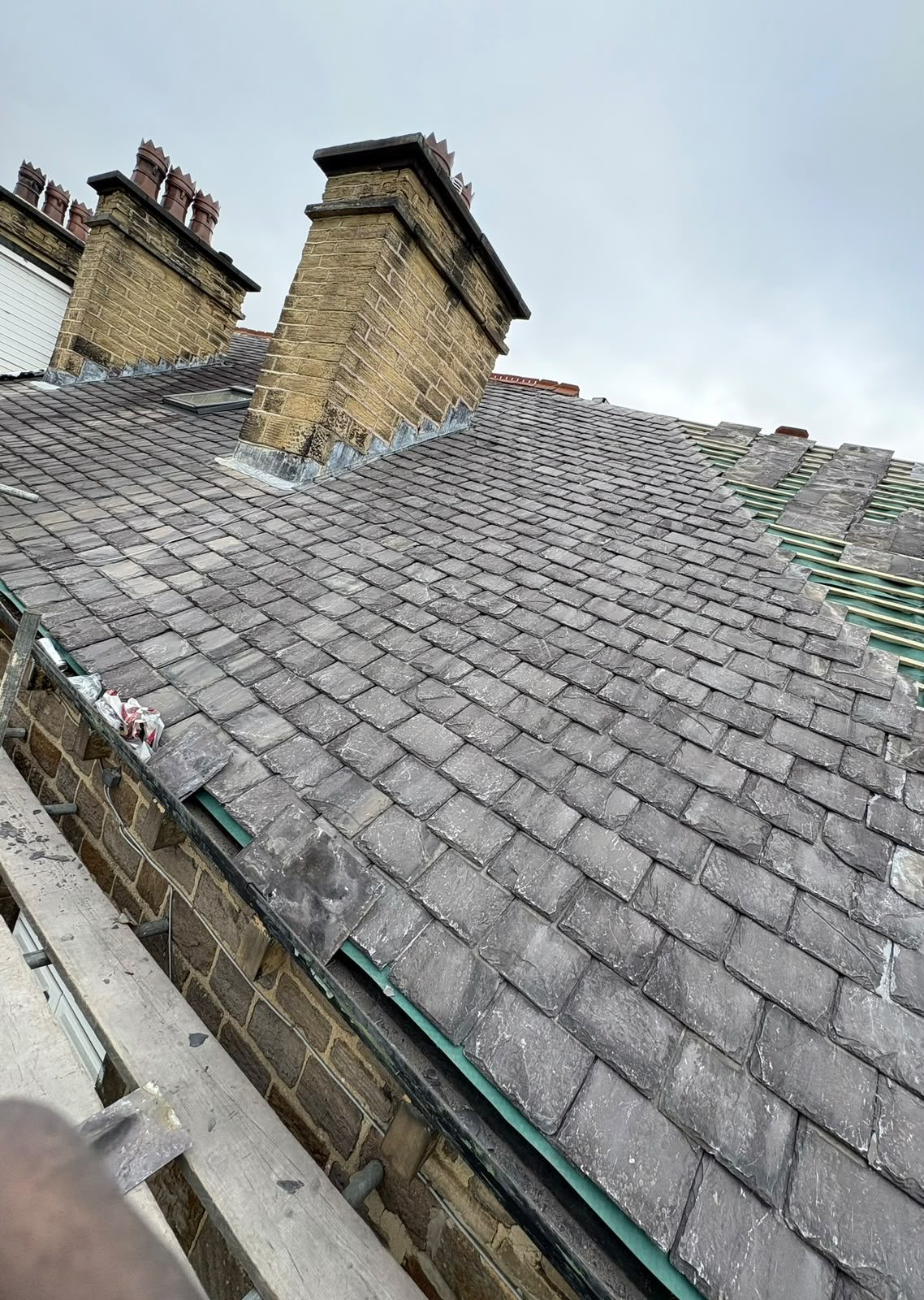 Slate roof being re-laid on a stone terrace, with new battens exposed alongside two stone chimney stacks