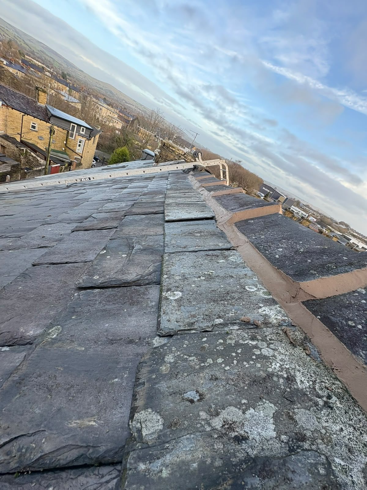 Ridge tiles re-bedded and repointed along a stone slate roof overlooking a Lancashire valley