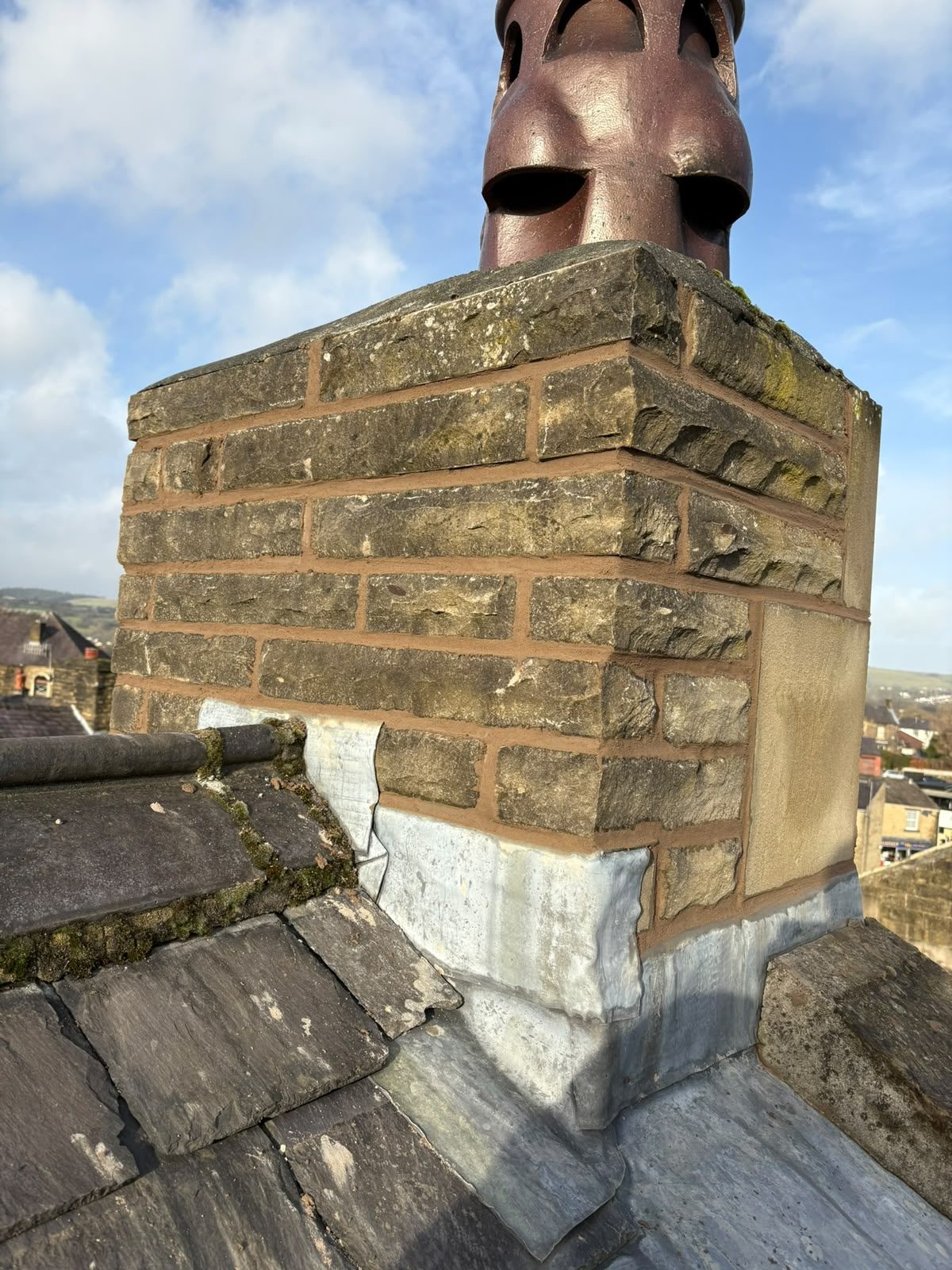 Stone chimney with clay pot and freshly dressed lead step flashing after chimney repointing work