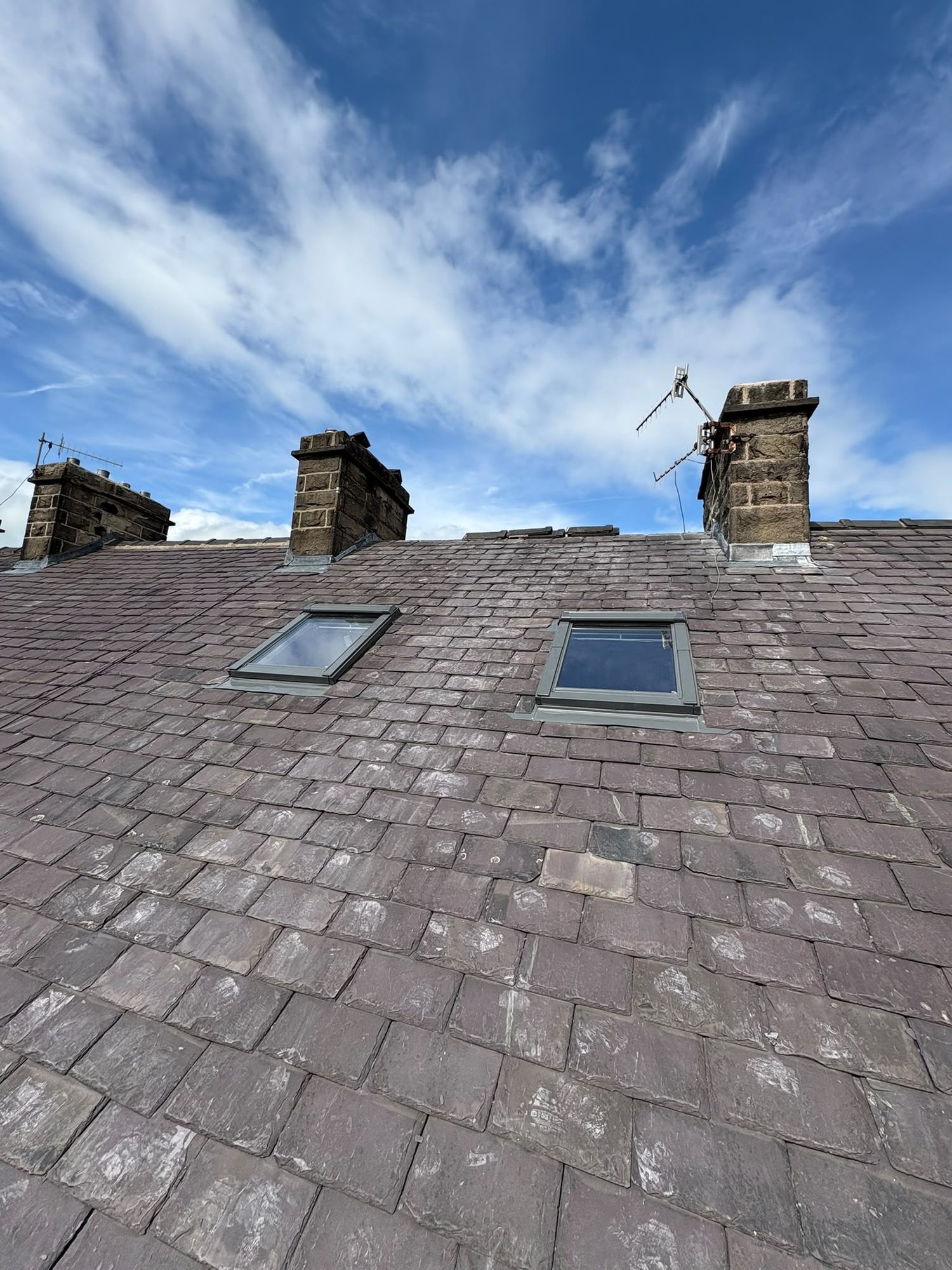 Completed slate roof with new roof windows and re-flashed stone chimneys against a blue sky