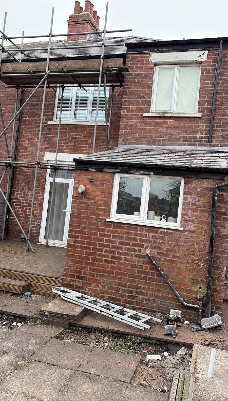 Rear elevation of a brick semi under scaffolding while roofline and guttering work is carried out
