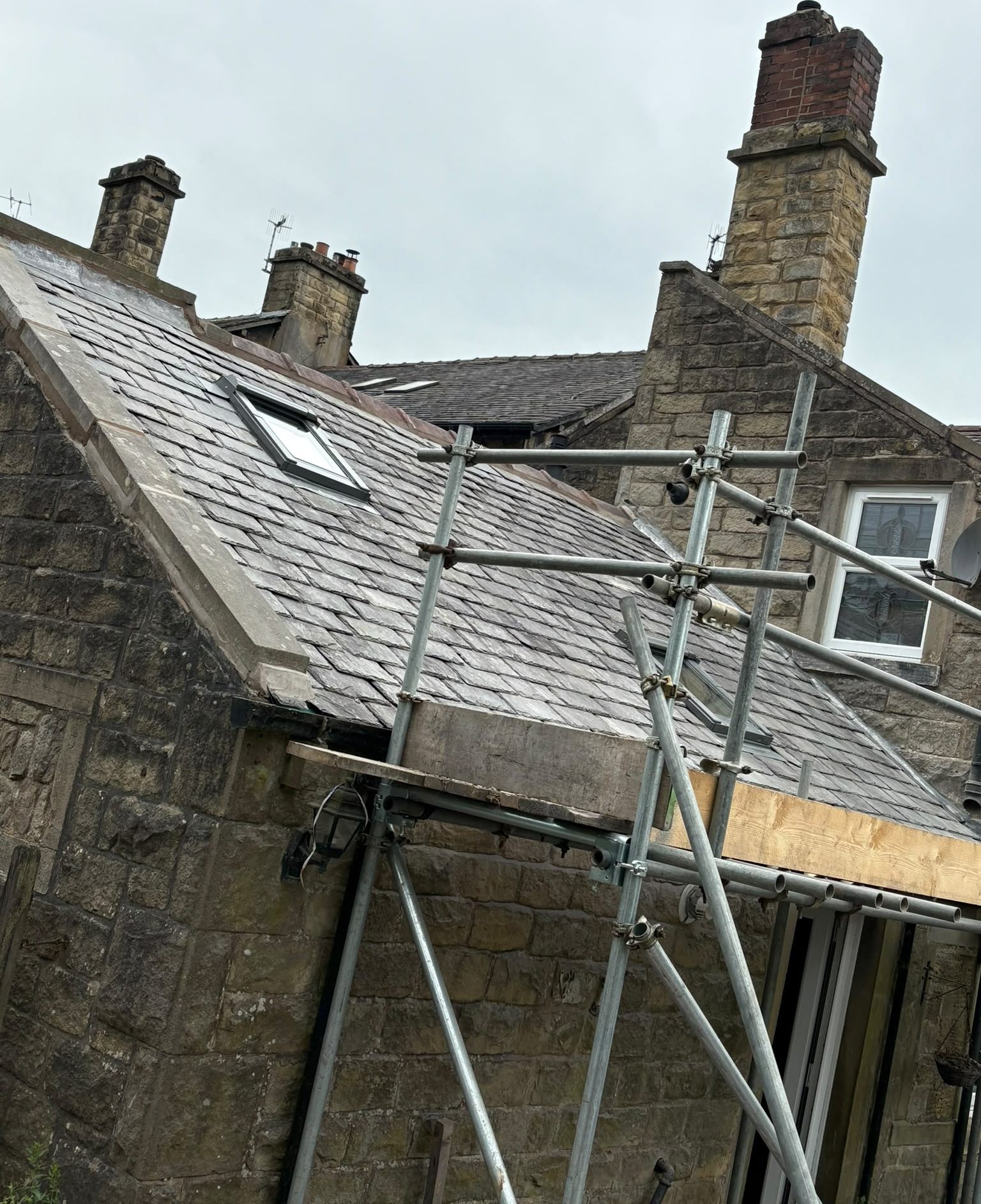 Slate roof and stone chimney stacks on a scaffolded property during roofing works